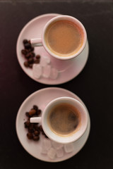Dwie białe porcelanowe filiżanki espresso z ziarnami kawy i kryształami cukru na spodkach