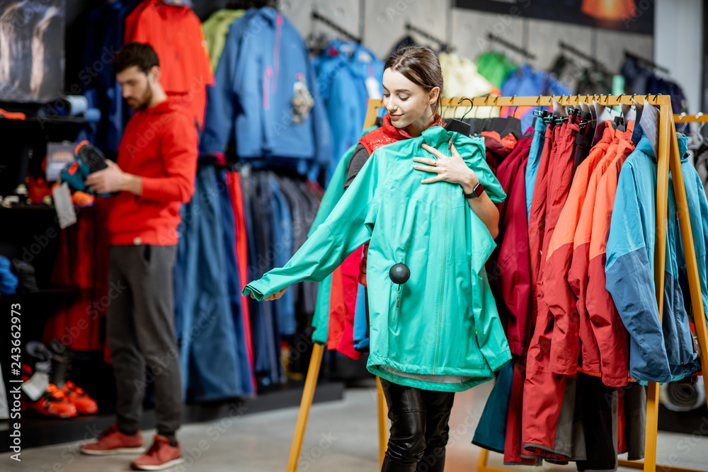 Wall mural Young woman choosing winter clothes trying windbreaking jacket in the sports shop