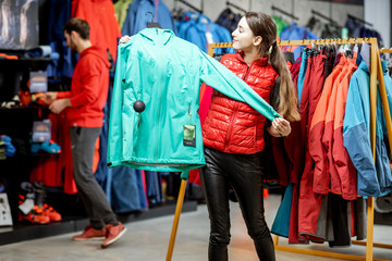 Young woman choosing winter clothes trying windbreaking jacket in the sports shop