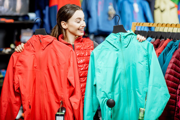 Young and cheerful woman choosing between red and turquoise jacket shopping in the sports store © rh2010