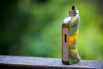 high end yellow green stabilized wood regulated box mods with rebuildable dripping atomizer on the old wood texture background, vaping device, selective focus