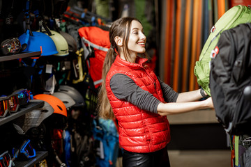 Young woman choosing some sports equipment looking on the backpacks in the sports shop