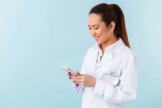 Woman Doctor Posing Isolated Over Blue Wall Background Using Mobile Phone.