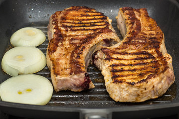 Steak of Large piece of pork meat with rib and onion prepared on a grill pan