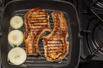 Steak of Large piece of pork meat with rib and onion prepared on a grill pan