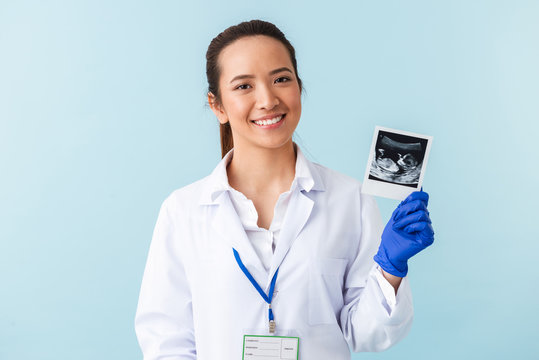 Woman doctor posing isolated over blue wall background holding x-ray of baby in hands.