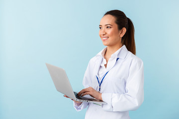 Young woman doctor posing isolated over blue wall background using laptop computer.