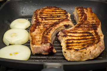 Steak of Large piece of pork meat with rib and onion prepared on a grill pan