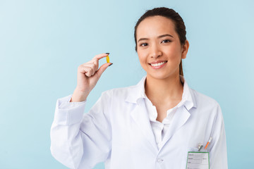 Young woman doctor posing isolated over blue wall background holding pills.