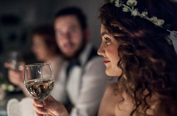 A close-up of a young bride sitting at a table on a wedding, holding a glass of wine.