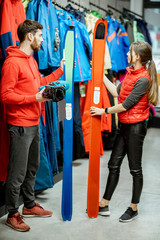 Man and woman choosing sports equipment looking on the ski and boots for skiing in the shop