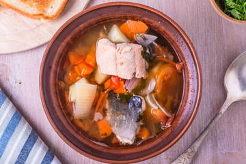 Chowder soup from salmon. Thick fish soup with potatoes, carrots and tomatoes in a clay plate. Top view.