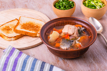 Thick fish soup with trout, potatoes, carrots and tomatoes in a clay plate on a rustic wooden table