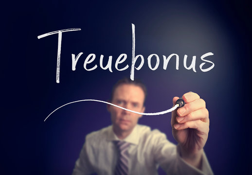 A businessman writing a Loyalty Bonus "Treuebonus" concept in German with a white pen on a clear screen.