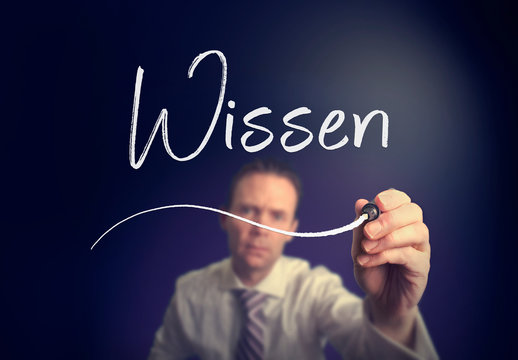 A businessman writing a Knowledge "Wissen" concept in German with a white pen on a clear screen.