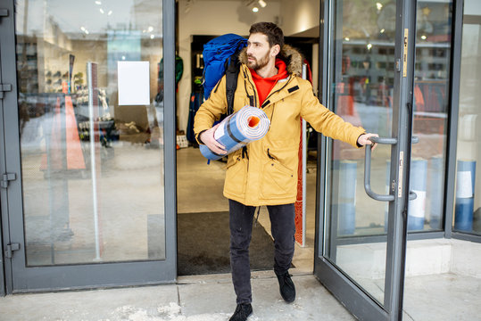 Happy Man Leaving Sports Shop With New Backpack And Camping Mat Standing In Front Of The Showcase Outdoors