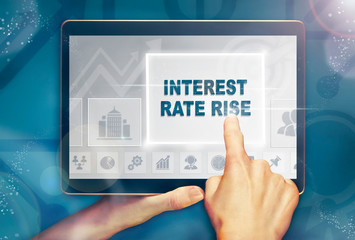 A hand selecting a Interest Rate Rise business concept on a computer tablet screen with a colorful background.