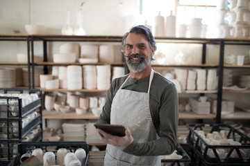 Smiling potter using tablet surrounded by work