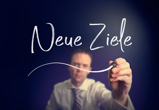 A businessman writing a New Goals "Neue Ziele" concept in German with a white pen on a clear screen.