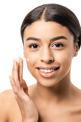 close-up view of beautiful young african american woman applying face cream and smiling at camera isolated on white