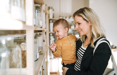 A young woman with a toddler boy buying groceries in zero waste shop.