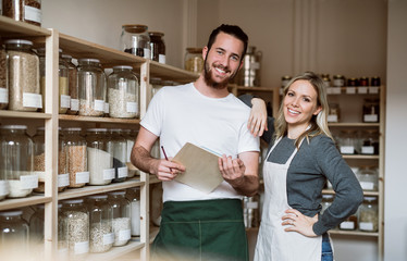 Two shop assistants standing in zero waste shop, checking stock.