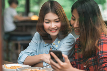 Fototapeta premium Happy beautiful Asian friends women blogger using smartphone photo and making food vlog video for her subscribers and her channel at cafe.