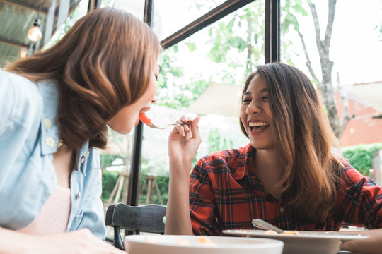 Beautiful happy Asian women lesbian lgbt couple sitting each side eating a plate of Italian seafood spaghetti and french fries at restaurant or cafe while smiling and looking at food.