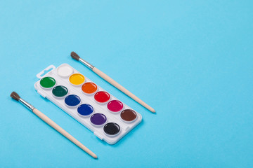 Watercolor paints and brushes in white box, isolated on blue background