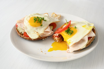 fried egg with running yolk on wholemeal bread rolls with tomato, cucumber and cooked ham, healthy hearty breakfast on a white table, copy space