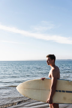 France, Brittany, young man carrying surfboard standing at the sea