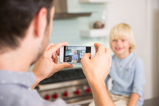 Father taking cell phone picture of son in kitchen