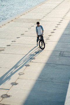 Young man with commuter fixie bike having a break on waterfront promenade at the riverside