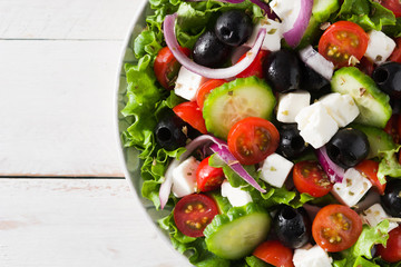 Fresh Greek salad in bowl with black olive,tomato,feta cheese, cucumber and onion on white wooden table. Close up