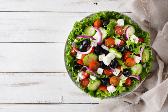 Fresh Greek salad in bowl with black olive,tomato,feta cheese, cucumber and onion on white wooden table. Top view. Copyspace