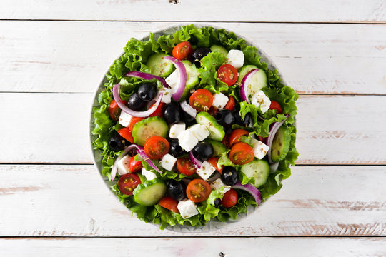 Fresh Greek salad in bowl with black olive,tomato,feta cheese, cucumber and onion on white wooden table. Top view. 