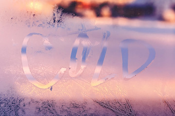 Word Cold on the frozen window glass. Hand written on the winter window