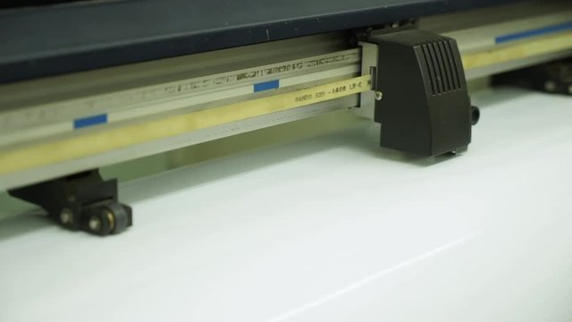 close view large format machine runner cuts fast pattern on white empty paper surface in typography