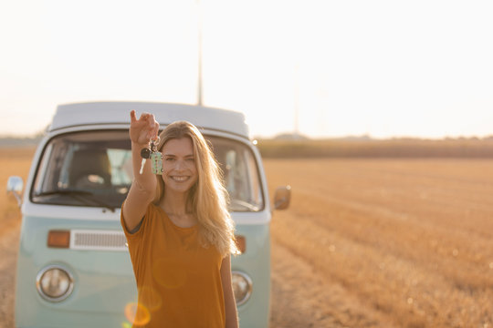 Happy young woman holding car key at camper van in rural landscape