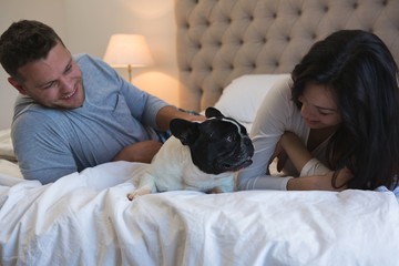 Couple playing with their pet dog in bedroom