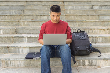 Male student sitting on stair steps and using laptop