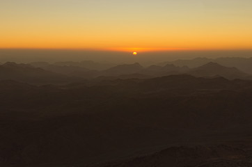 Naklejka na ściany i meble Scenic sunrise in the mountains. The sun comes out from the cloud. View from Mount Sinai (Mount Horeb, Gabal Musa, Moses Mount). Sinai Peninsula of Egypt