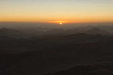 Magic golden sunrise in the mountains. The sun comes out from the cloud. View from Mount Sinai (Mount Horeb, Gabal Musa, Moses Mount). Sinai Peninsula of Egypt