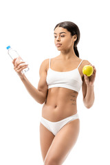 slim young african american woman in underwear holding bottle of water and green apple isolated on white