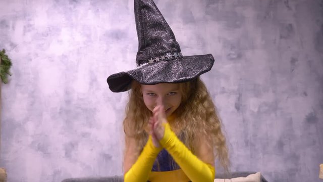 Stargazer girl rubs hands. Close up front view little witch viciously rubs her hands, ready to cast a spell wizard Helloween hat. Wish warlock close up front view