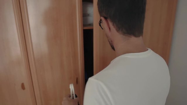 Single man is pulling out hanger with clothes and going to mirror in morning