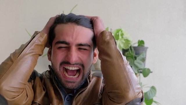 Young man holds his head with his hands as she screams in pain and disgust and frustration with his problems and the incompetence around him  