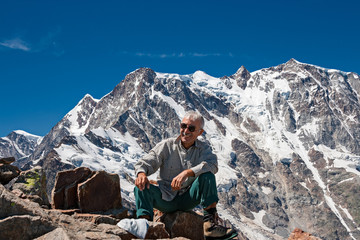 A mountaineer smiles satisfied with the climb, in the background the peaks of the imposing east face of Monte Rosa above Macugnaga in Piedmont, Italy.