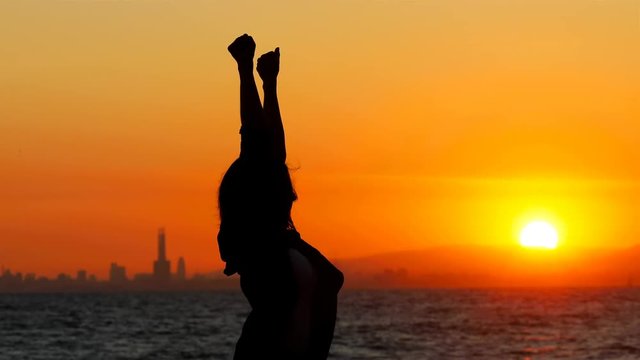 Backlight silhouette of an excited woman celebrating success jumping at sunset