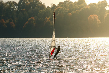 Windusrfer in the sunset. Man windsurfing with on board in beautiful sunlight